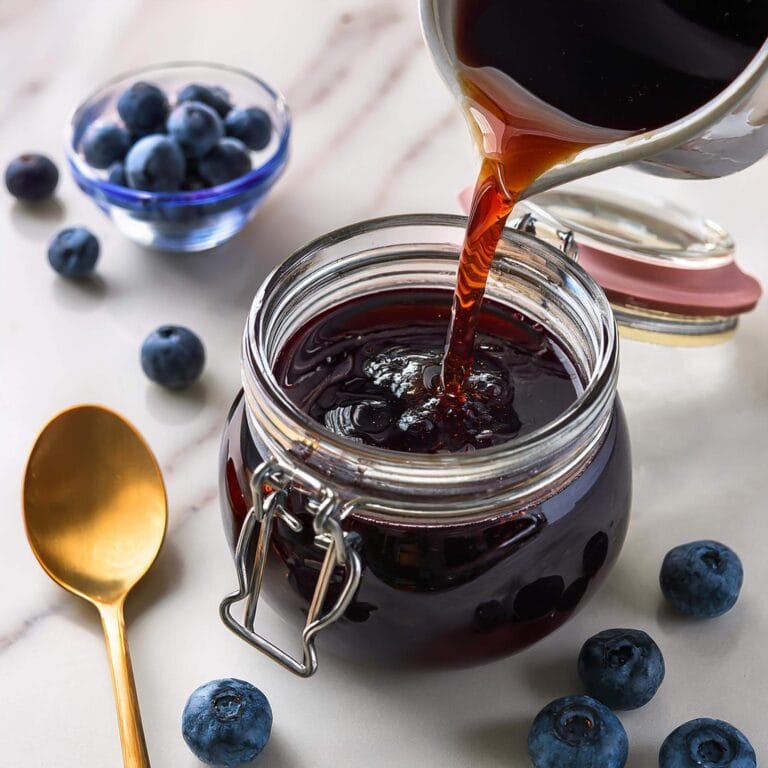 syrup Fresh blueberry being poured into a glass jar on a marble surface.