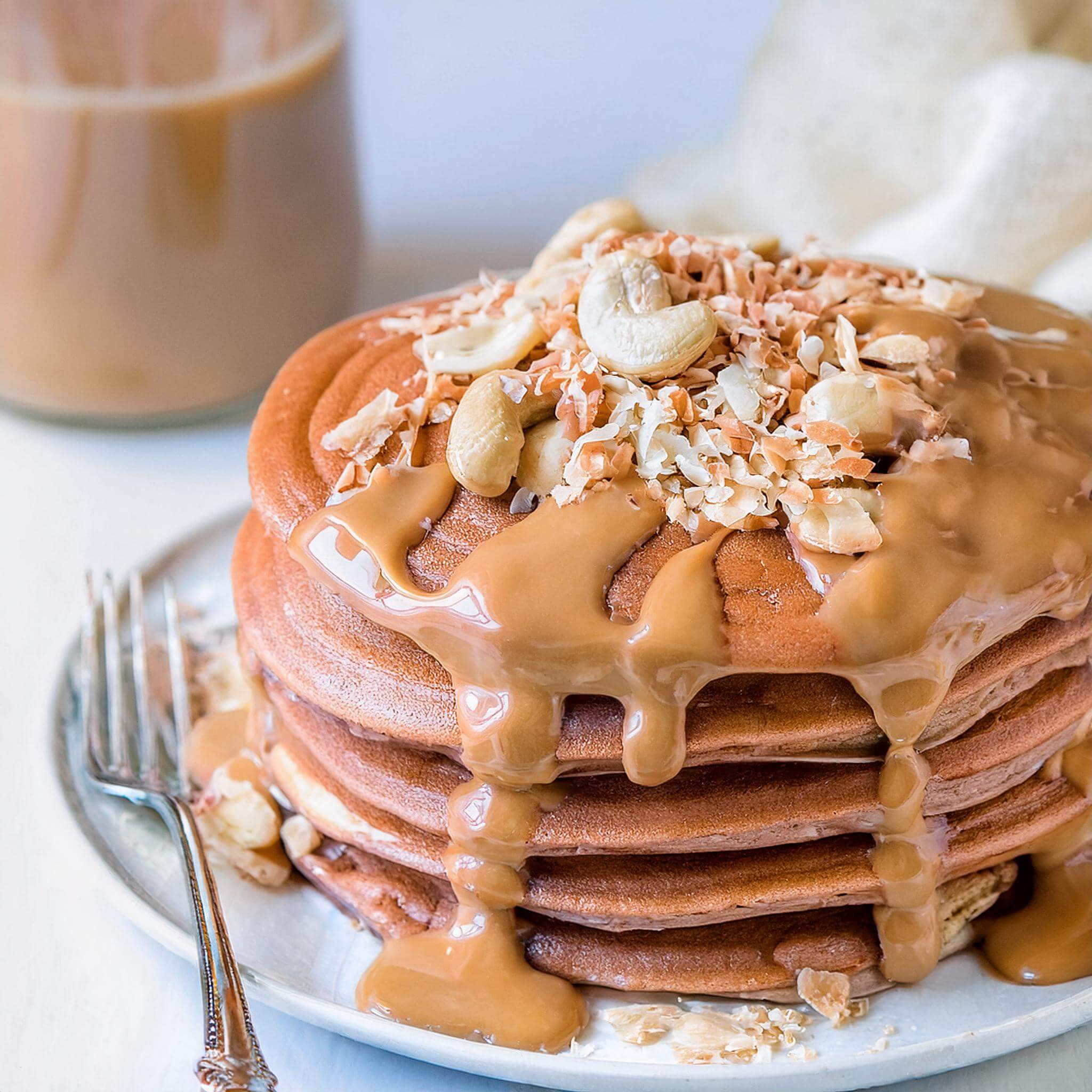 Pancake stack topped with peanut butter, cashews, and toasted coconut.