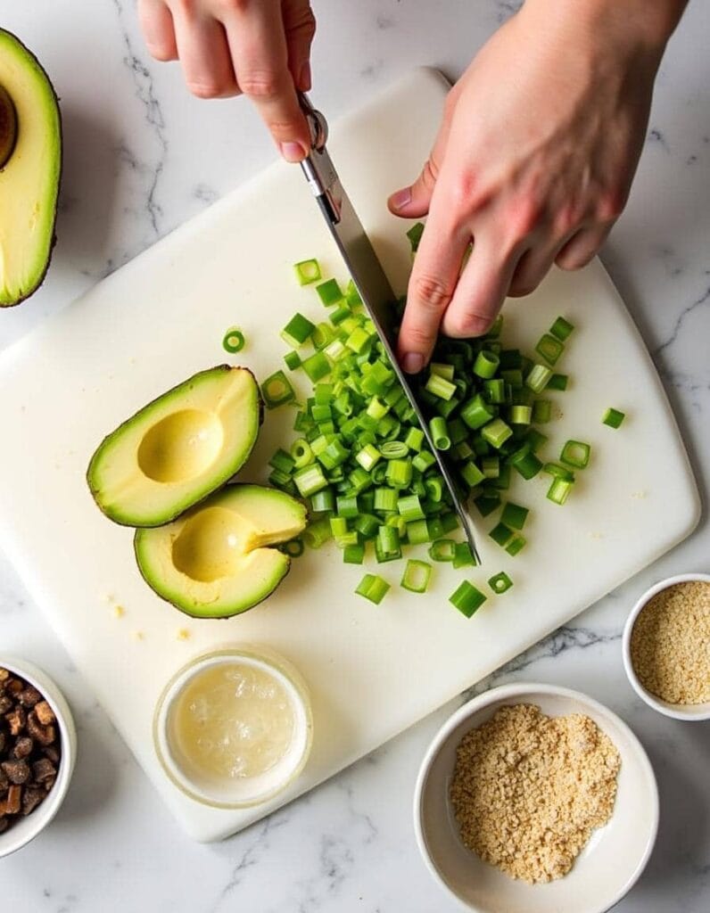 Hands preparing avocado slices and green onions for garnishing a salmon rice bowl.