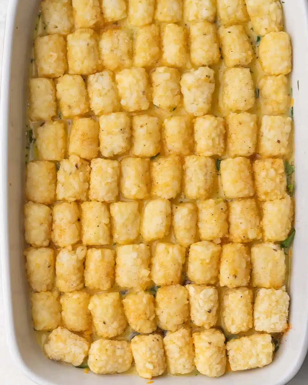 Tater Tot casserole before baking, topped with cheese.