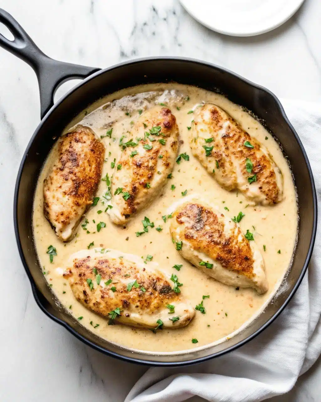 Golden-brown chicken breasts simmering in a rich and creamy garlic Parmesan sauce in a pan.