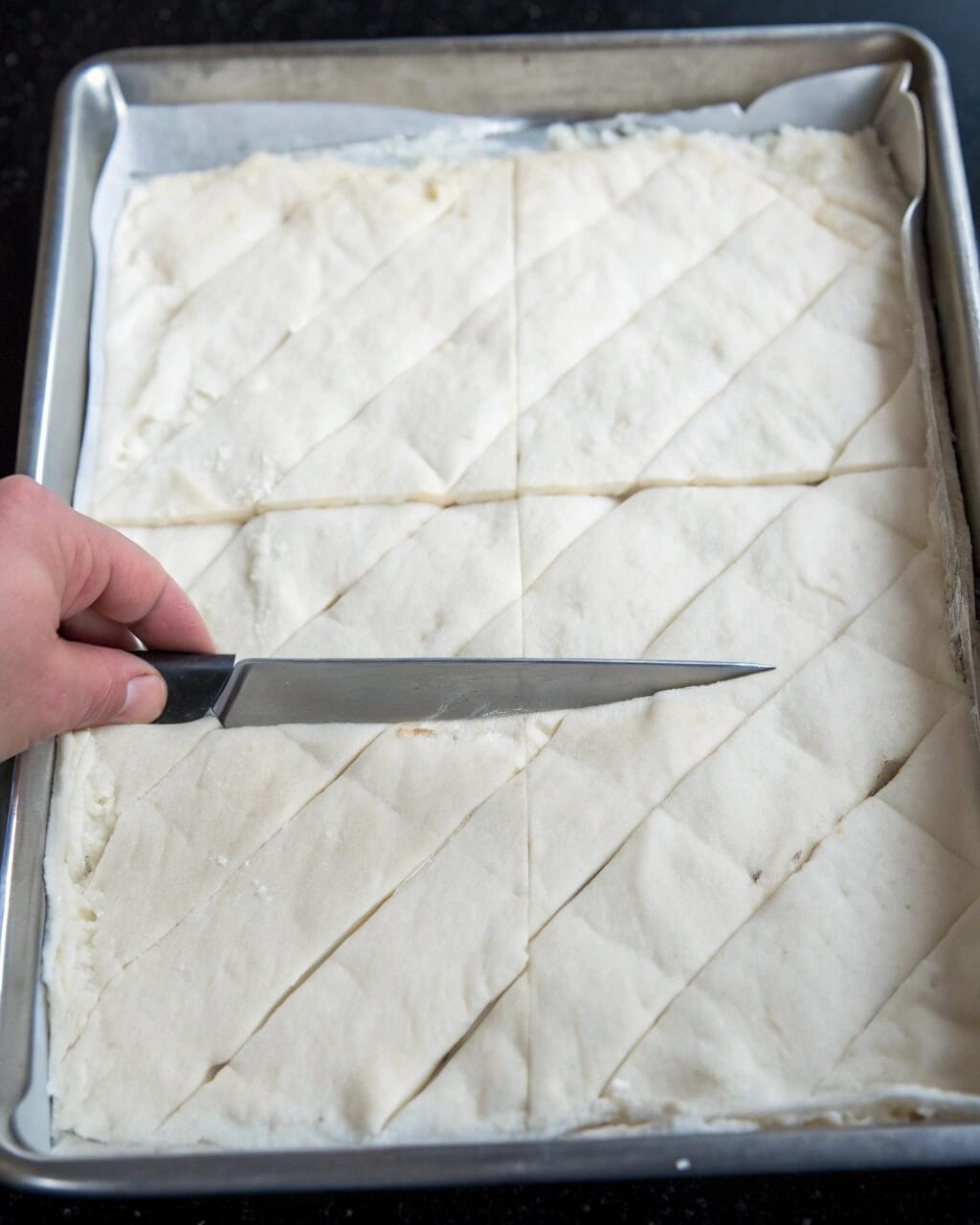 Cutting golden baklava into diamond-shaped pieces on a white kitchen counter.