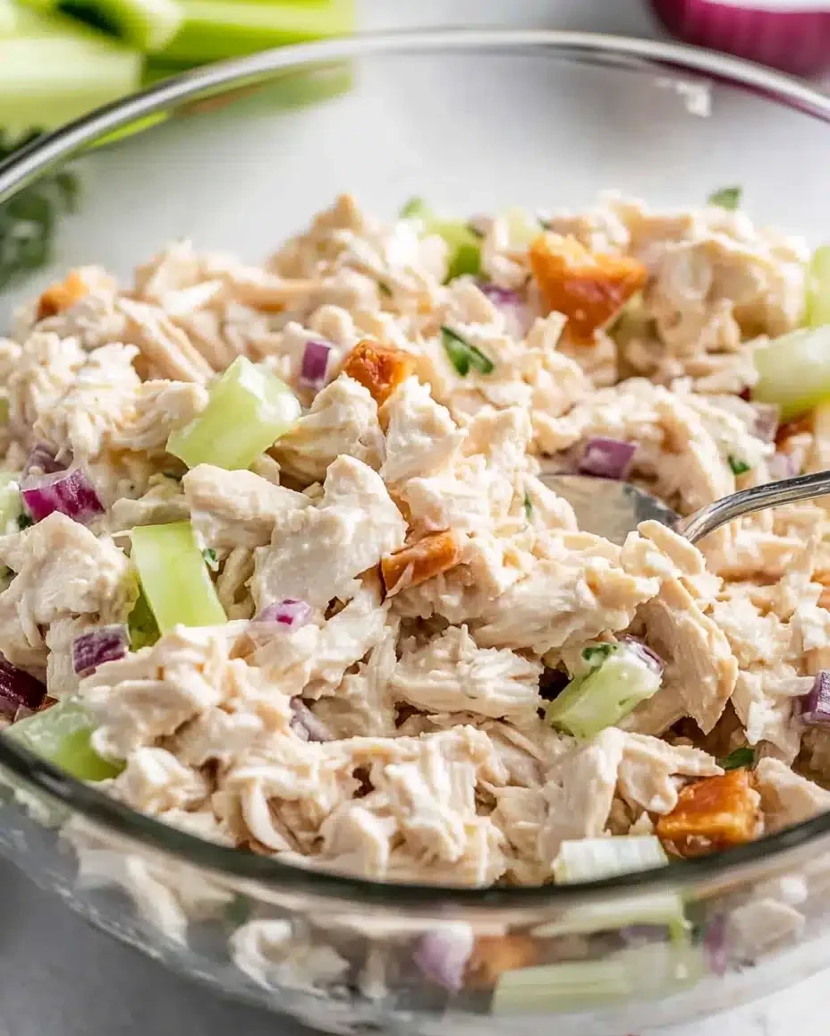 Mixing shredded chicken with mayo, herbs, and vegetables in a bowl.